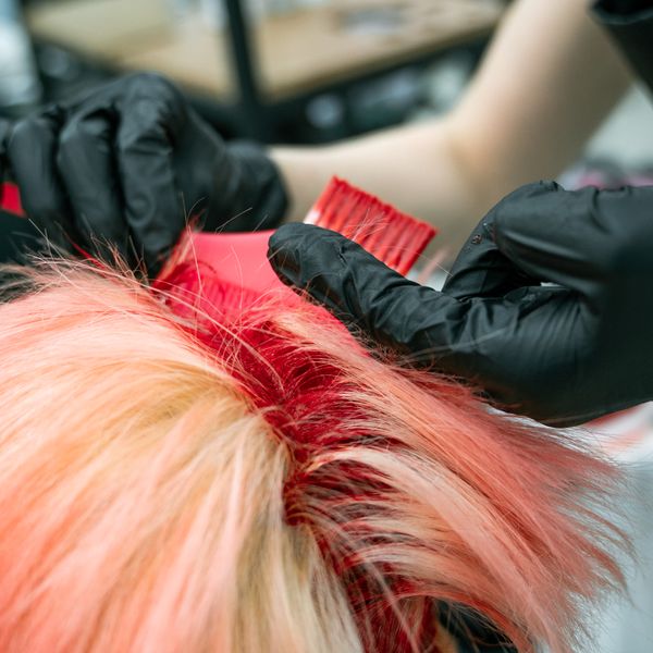 Vivid red-pink colour being separated into sections at the root on blonde hair