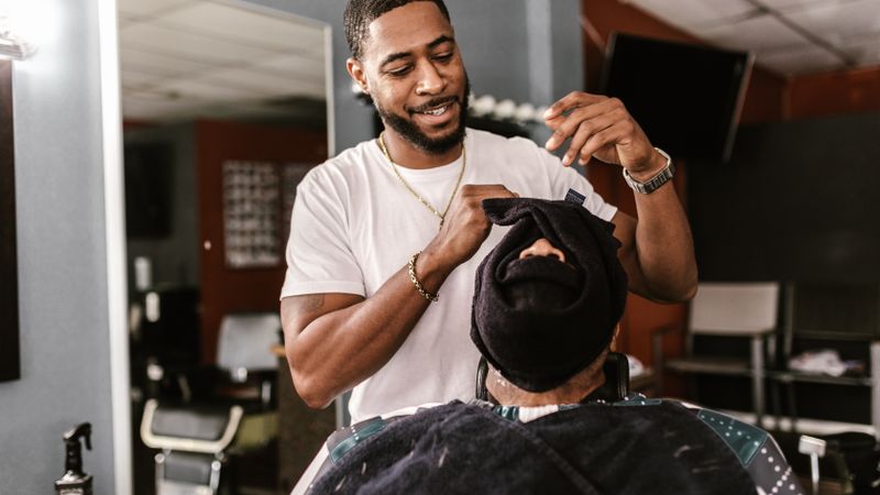 A barber tending to a seated client during a hot-towel shave
